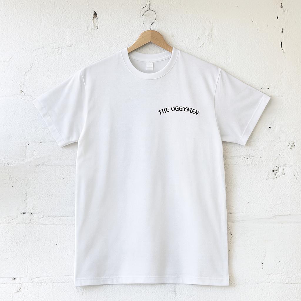 White t-shirt with 'THE OGGYMEN' text on a wooden hanger against a textured white wall.