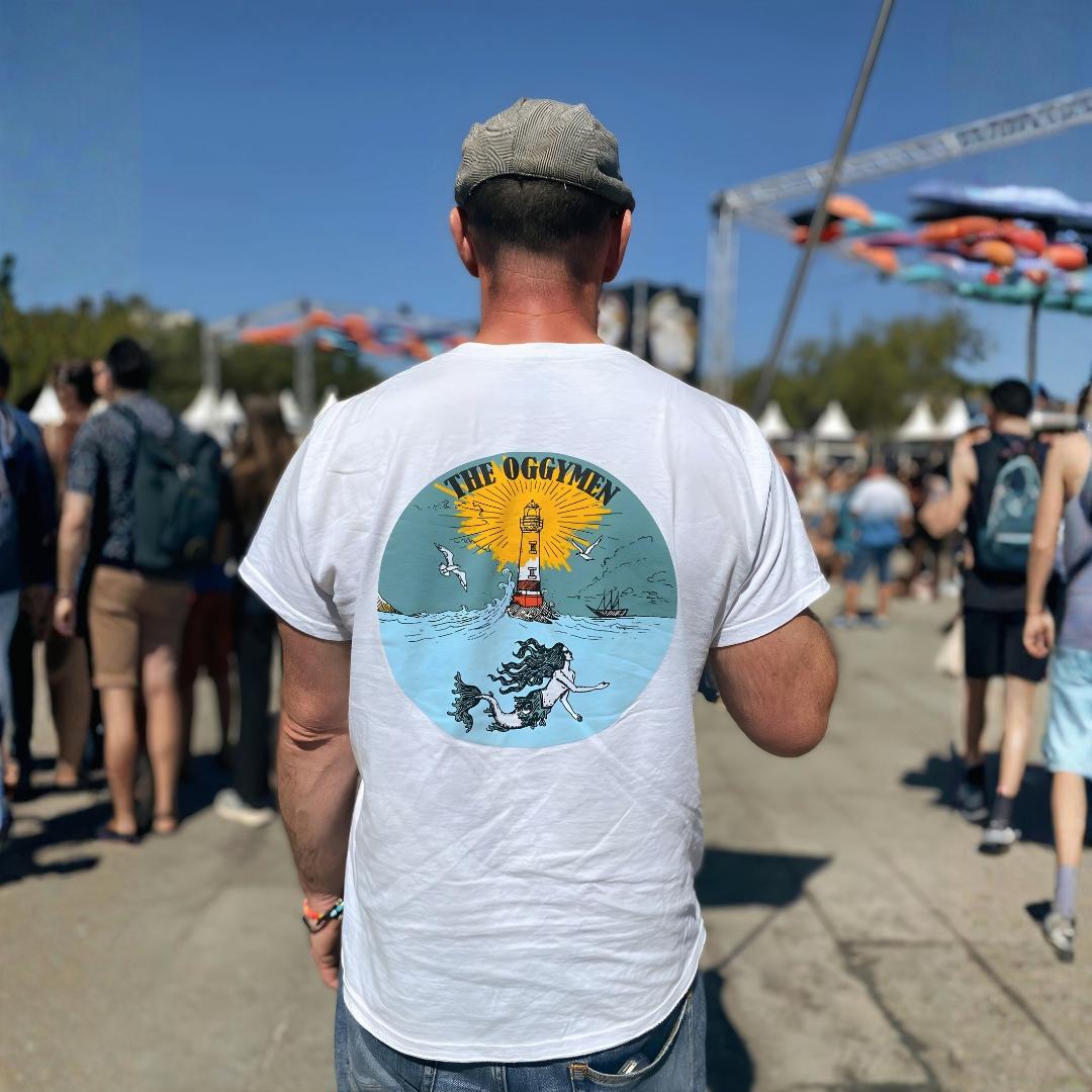 Man wearing a white t-shirt with a colorful graphic on the back at an outdoor event.