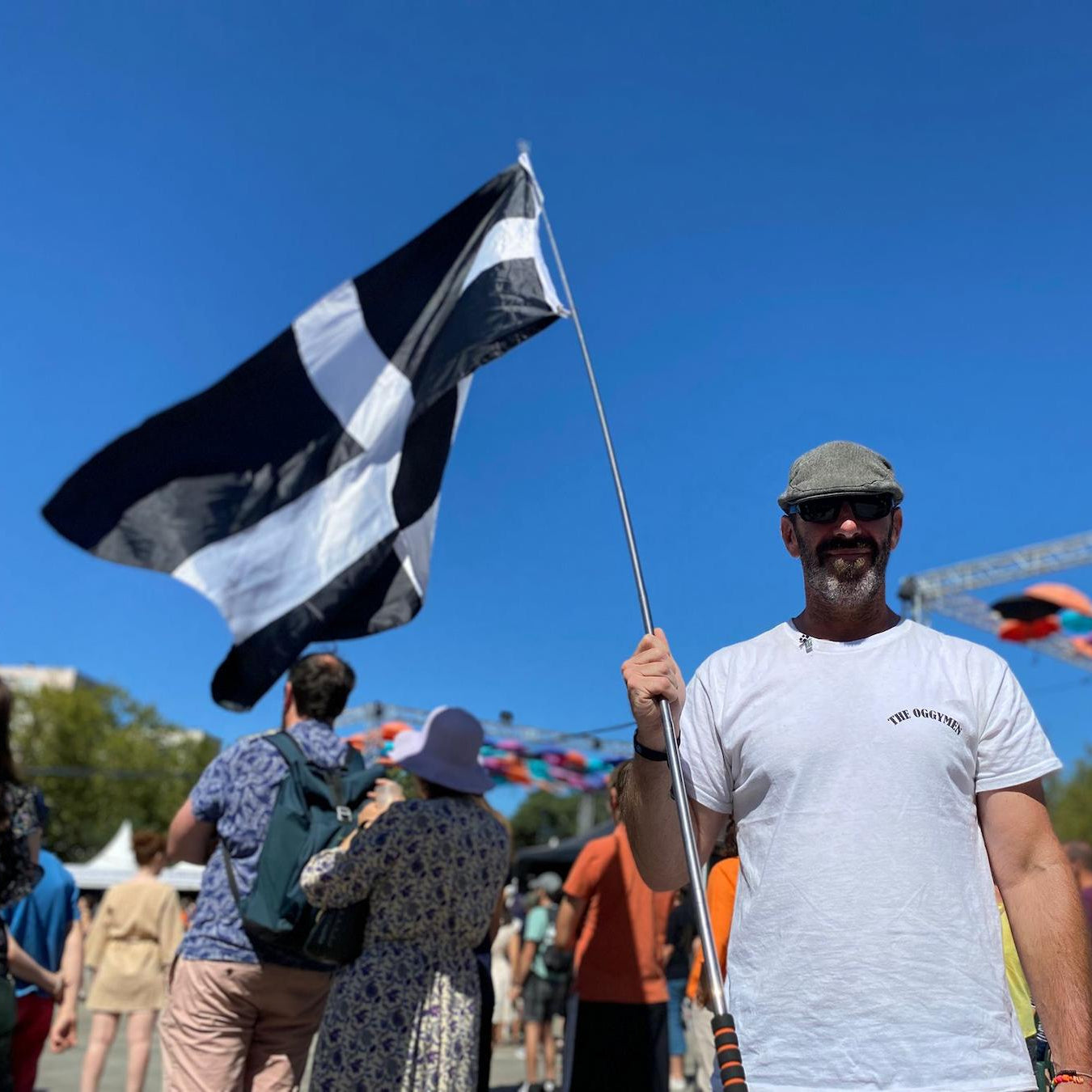 Man holding a black and white flag at an outdoor event with colorful inflatables in the background.